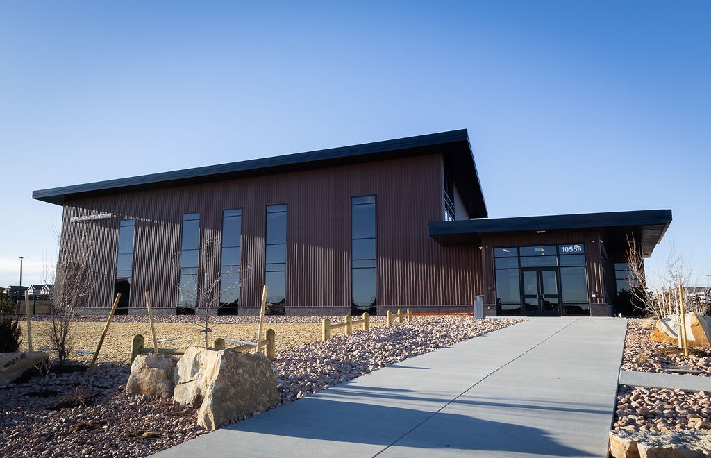 A modern building with large windows, a flat roof, and a pathway leading to the entrance, surrounded by landscaped rocks.