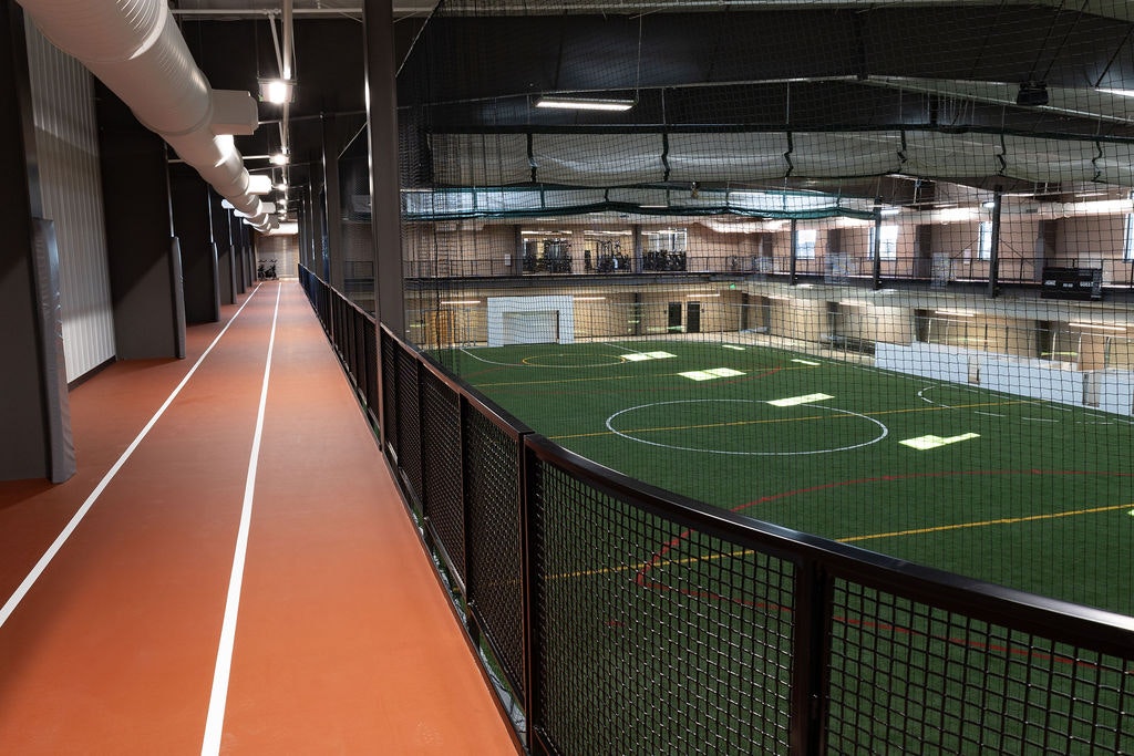 A spacious indoor sports facility with a running track above a multi-use field, featuring turf and marked lines for games.