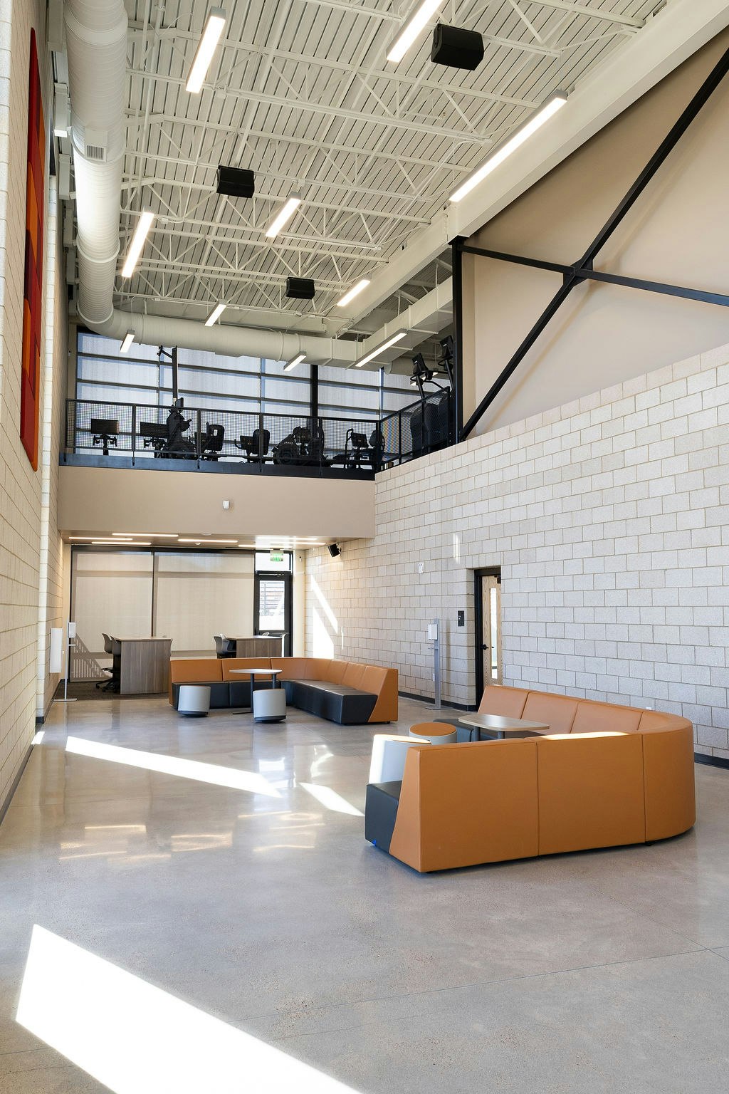 A spacious, modern lobby with a mix of seating, natural light, and a fitness area visible on an upper level.