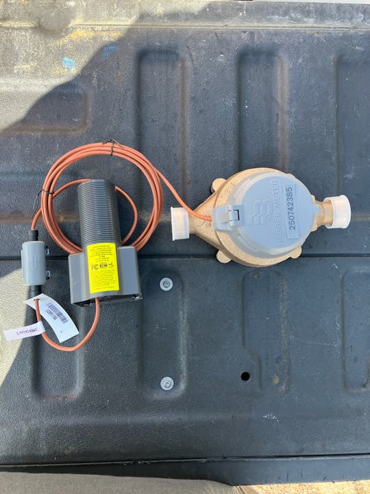 A water meter with a connected device and wire, labeled "BADGER METER" on a textured gray surface.