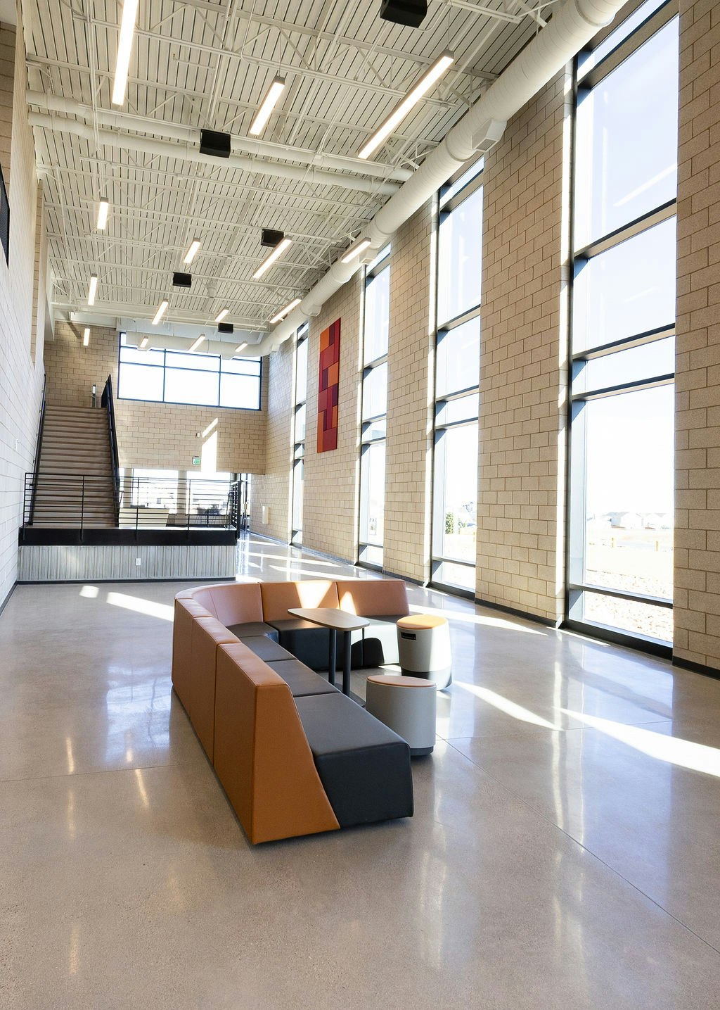 A spacious, modern room with large windows, a stylish seating area, and a staircase, featuring bright lighting and minimal decor.