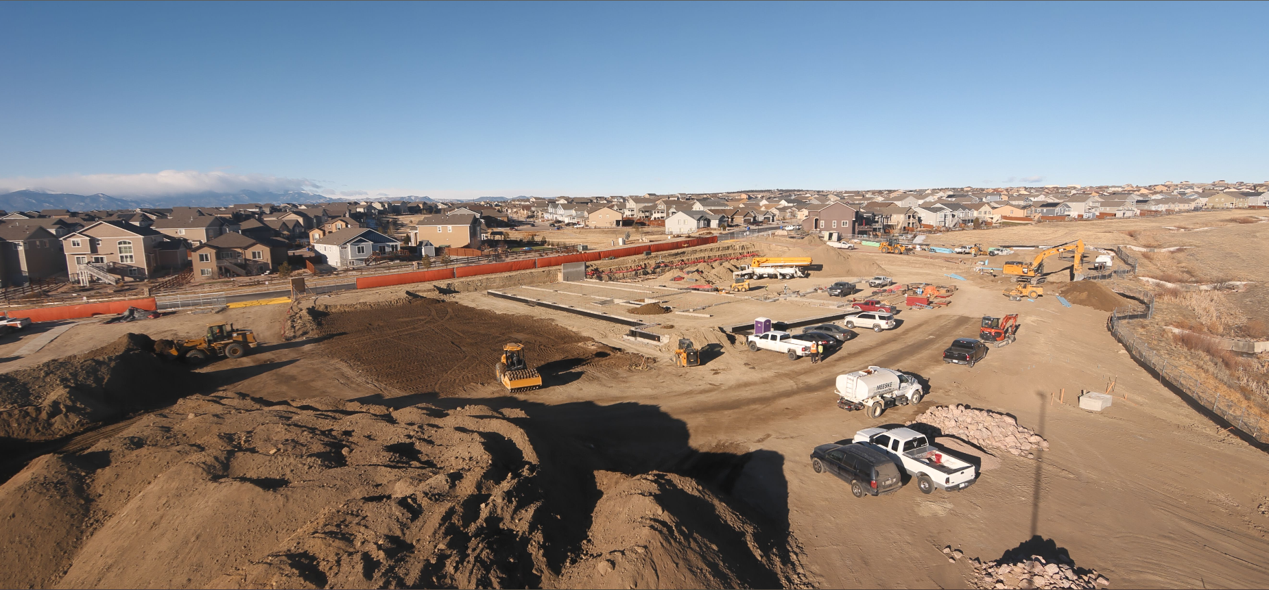 A construction site with various vehicles, equipment, and houses in the background.