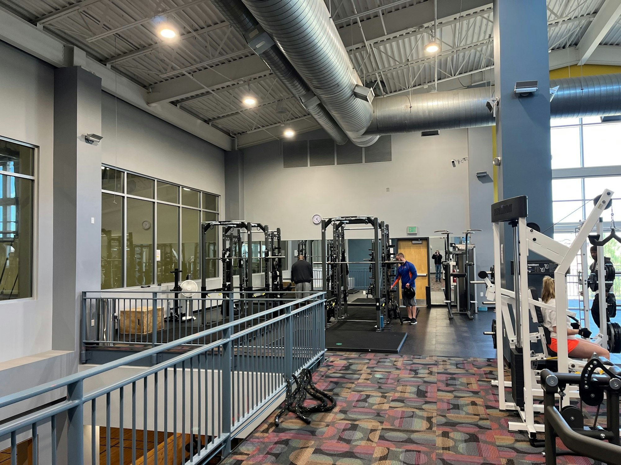 A spacious gym interior featuring exercise equipment, weightlifting racks, and a few people working out on different machines.