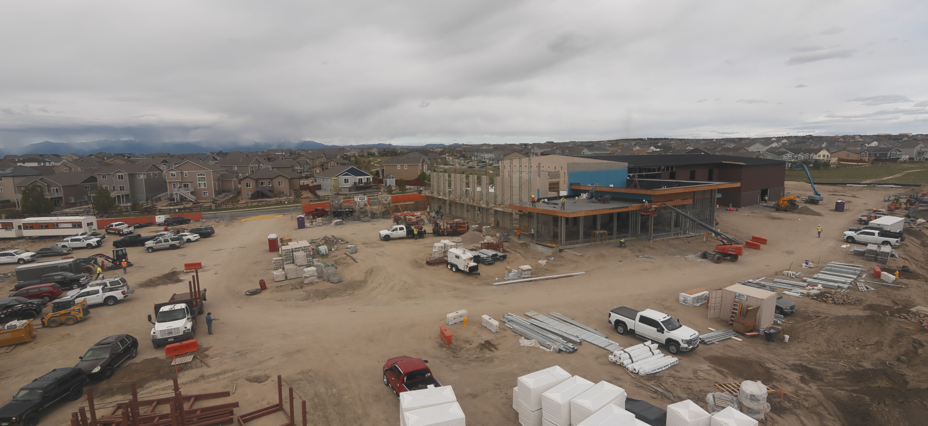 Construction site with building materials, vehicles, and equipment around a partially built structure in a residential area.