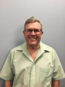 A person wearing glasses and a light green shirt is smiling against a plain gray background.