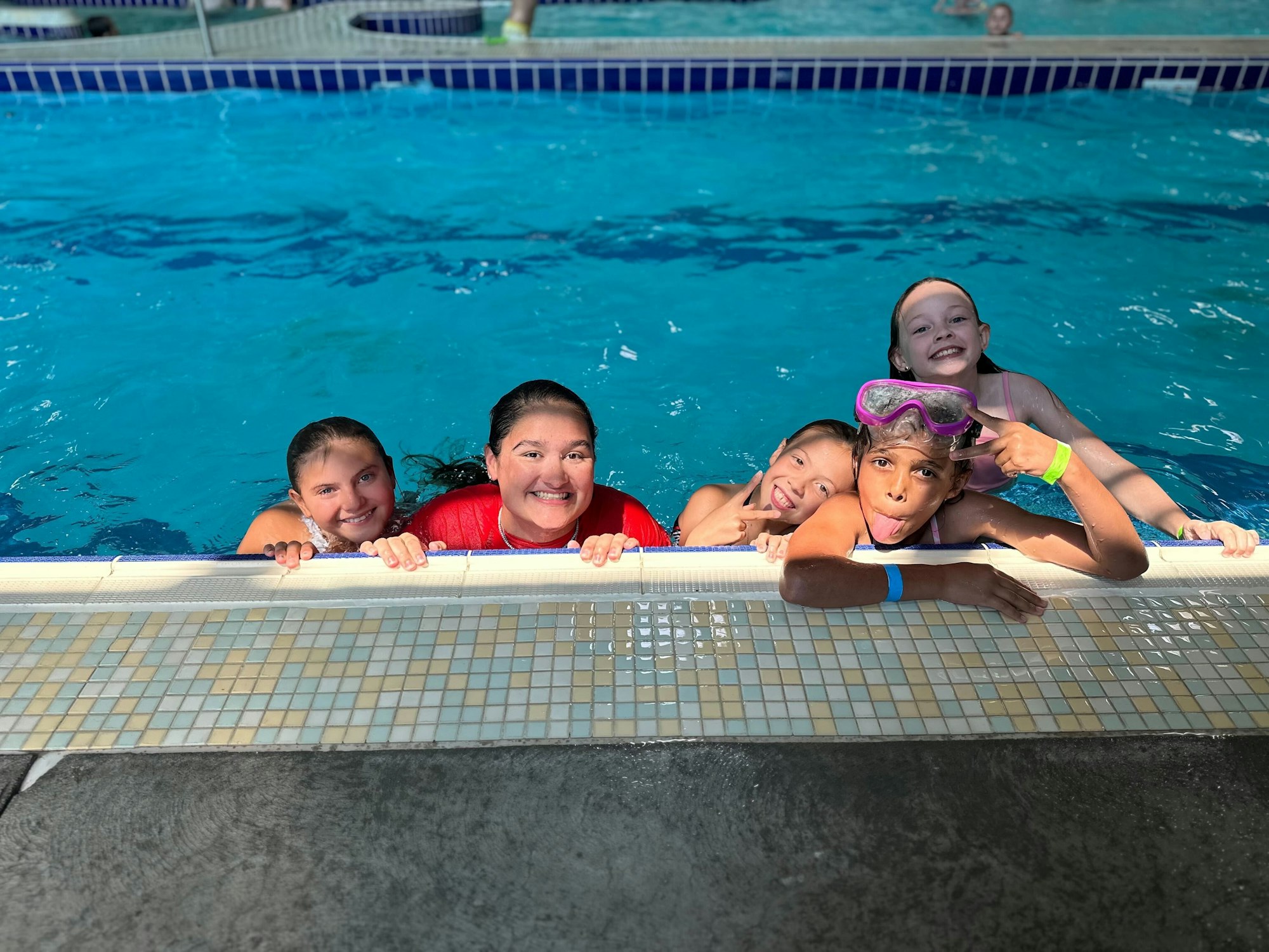 Five people smiling and posing in a swimming pool, holding onto the edge.