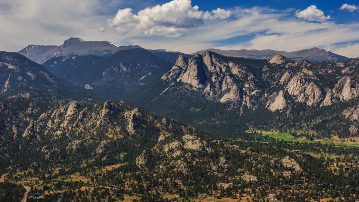 A breathtaking landscape featuring mountains, rocky formations, and lush greenery under a bright blue sky with clouds.