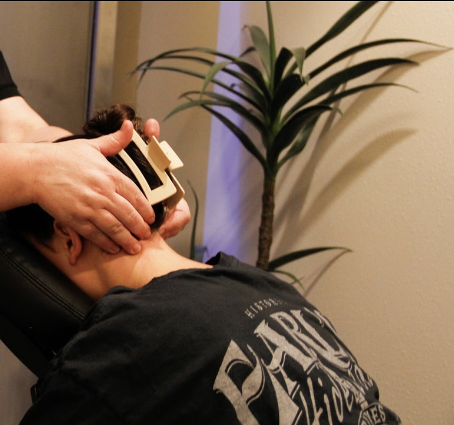 A person receiving a neck adjustment with a wooden tool, while lying on a table, near a plant.