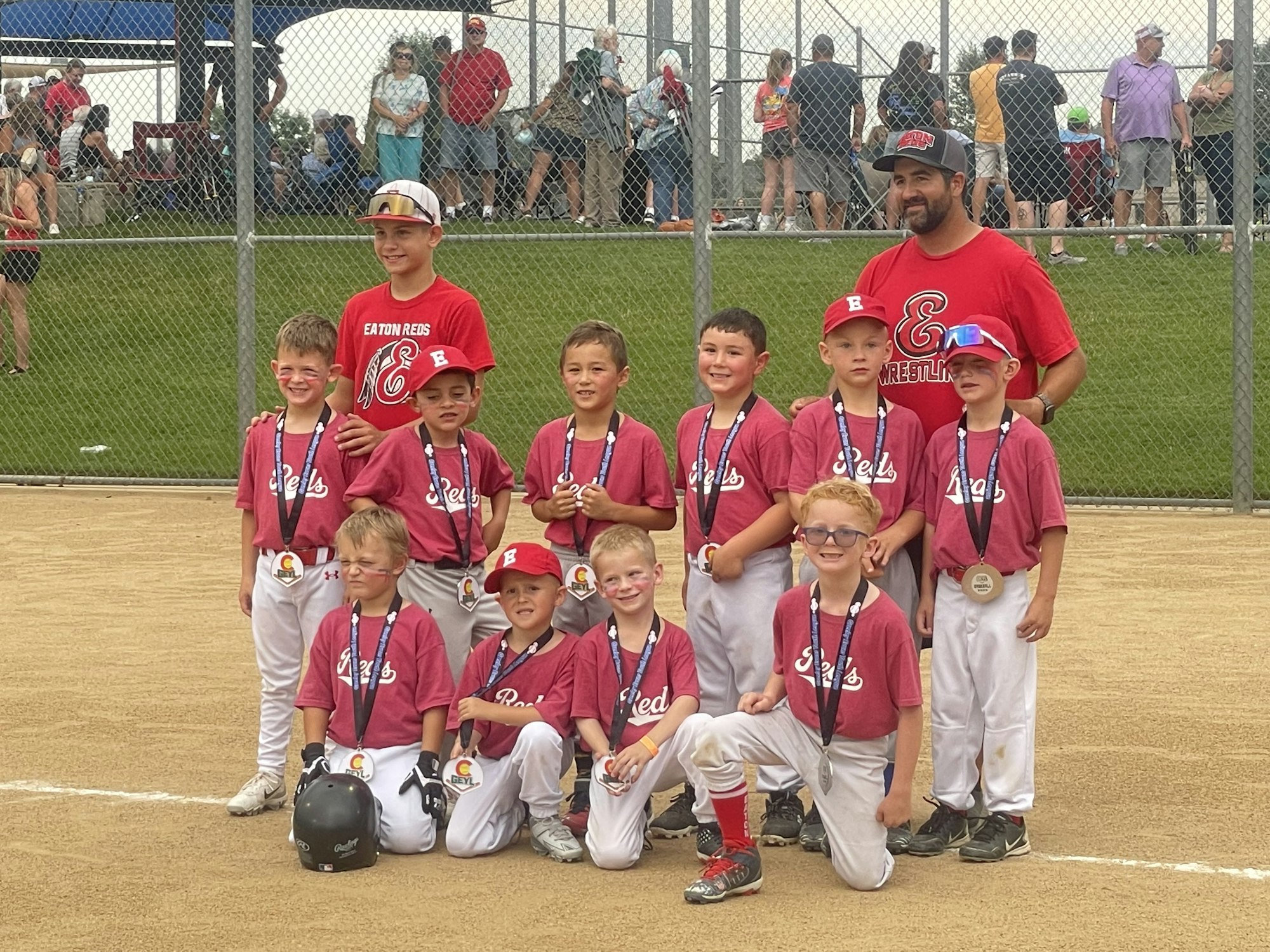 Youth baseball team with medals and a coach posing on a field.