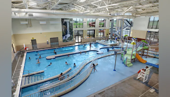 The image shows an indoor swimming pool complex with people swimming, water slides, and play equipment for kids.