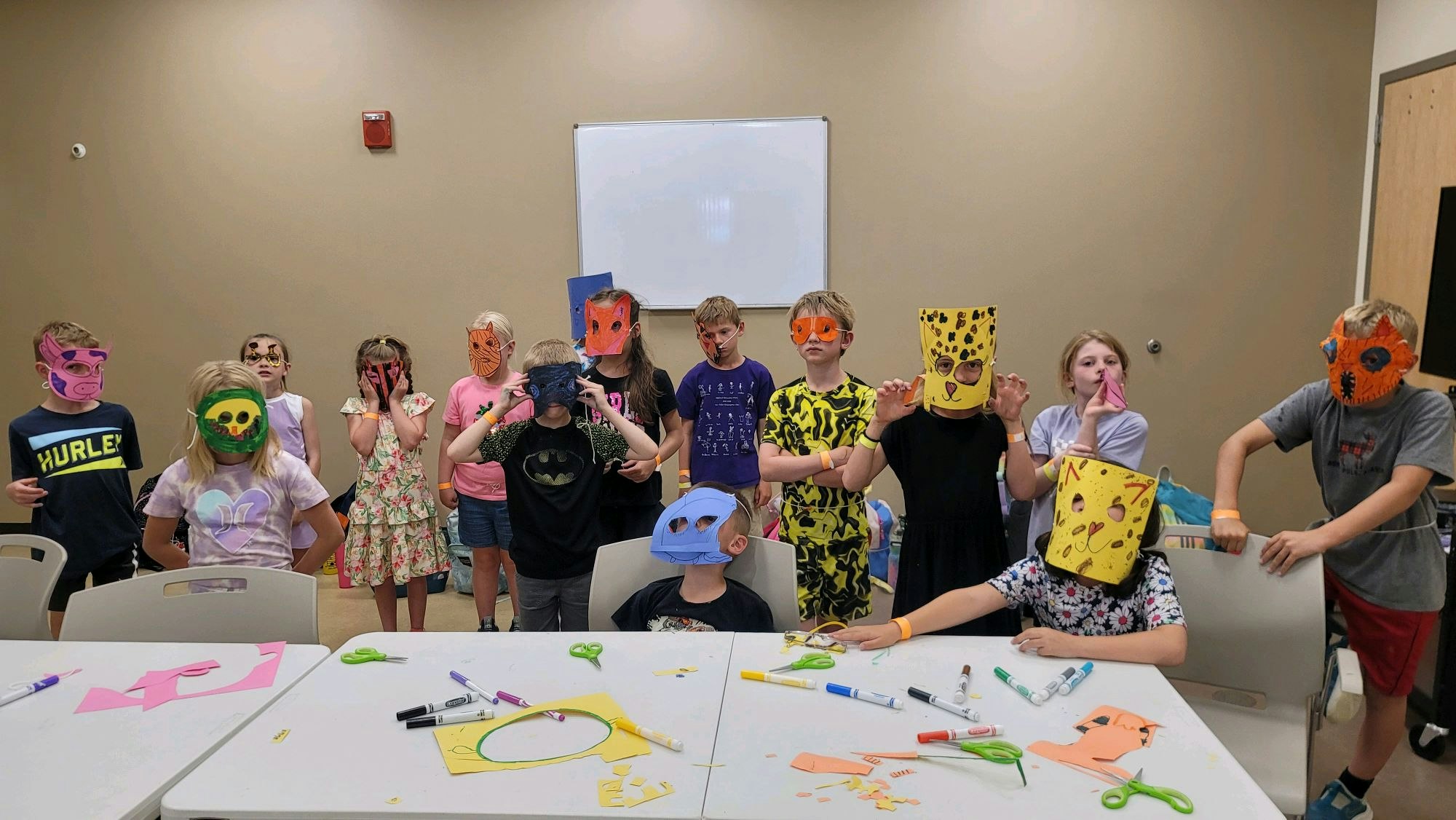 Children wearing colorful animal masks, standing in a classroom with art supplies on tables.