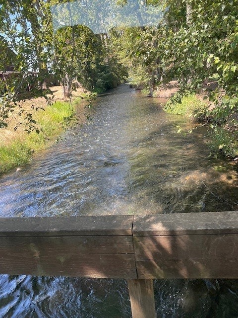 A serene river flowing under a wooden bridge, surrounded by lush green trees and grass.