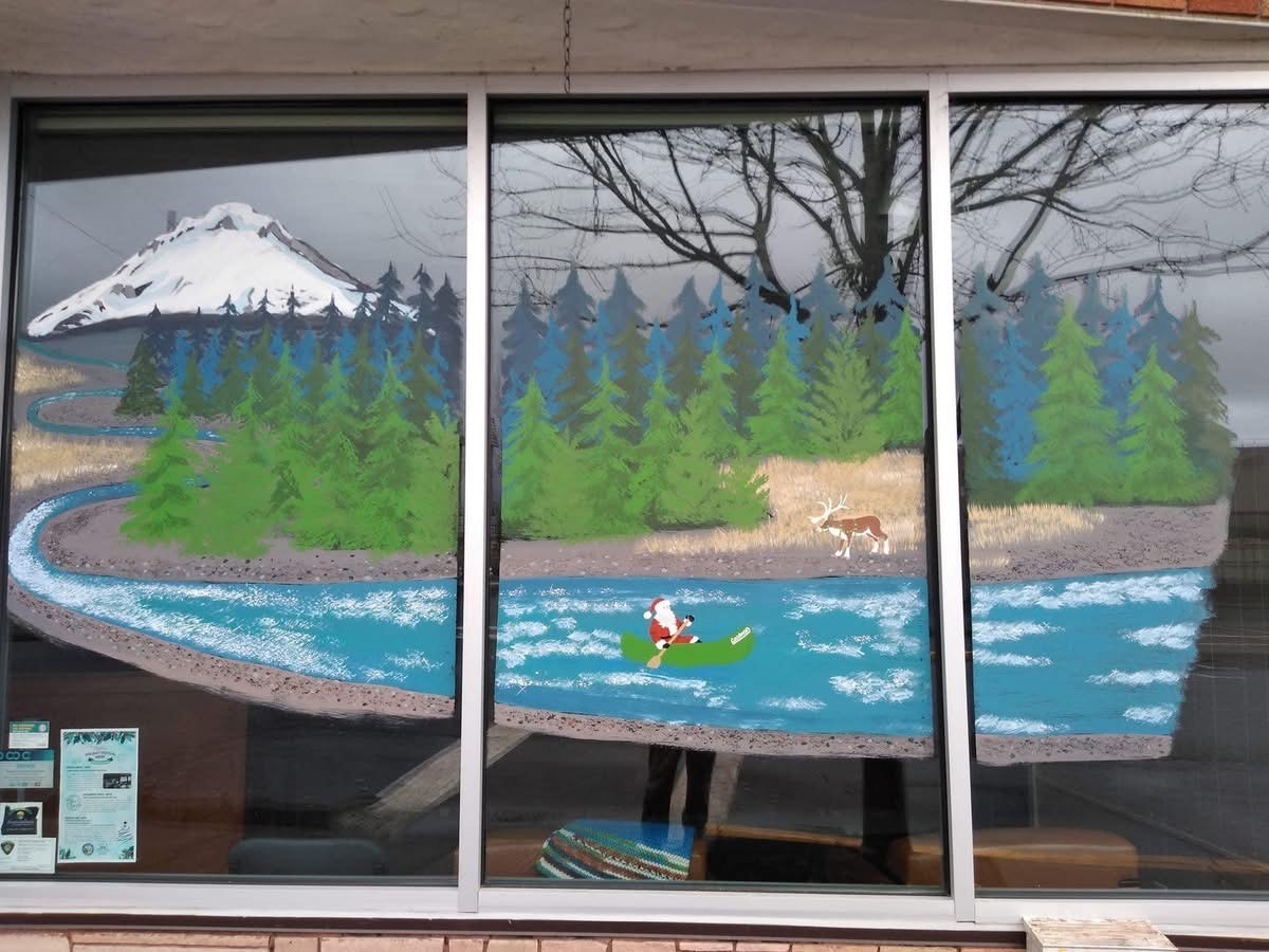 A painted window scene with a snowcapped mountain, river, forest, person kayaking, and a deer.