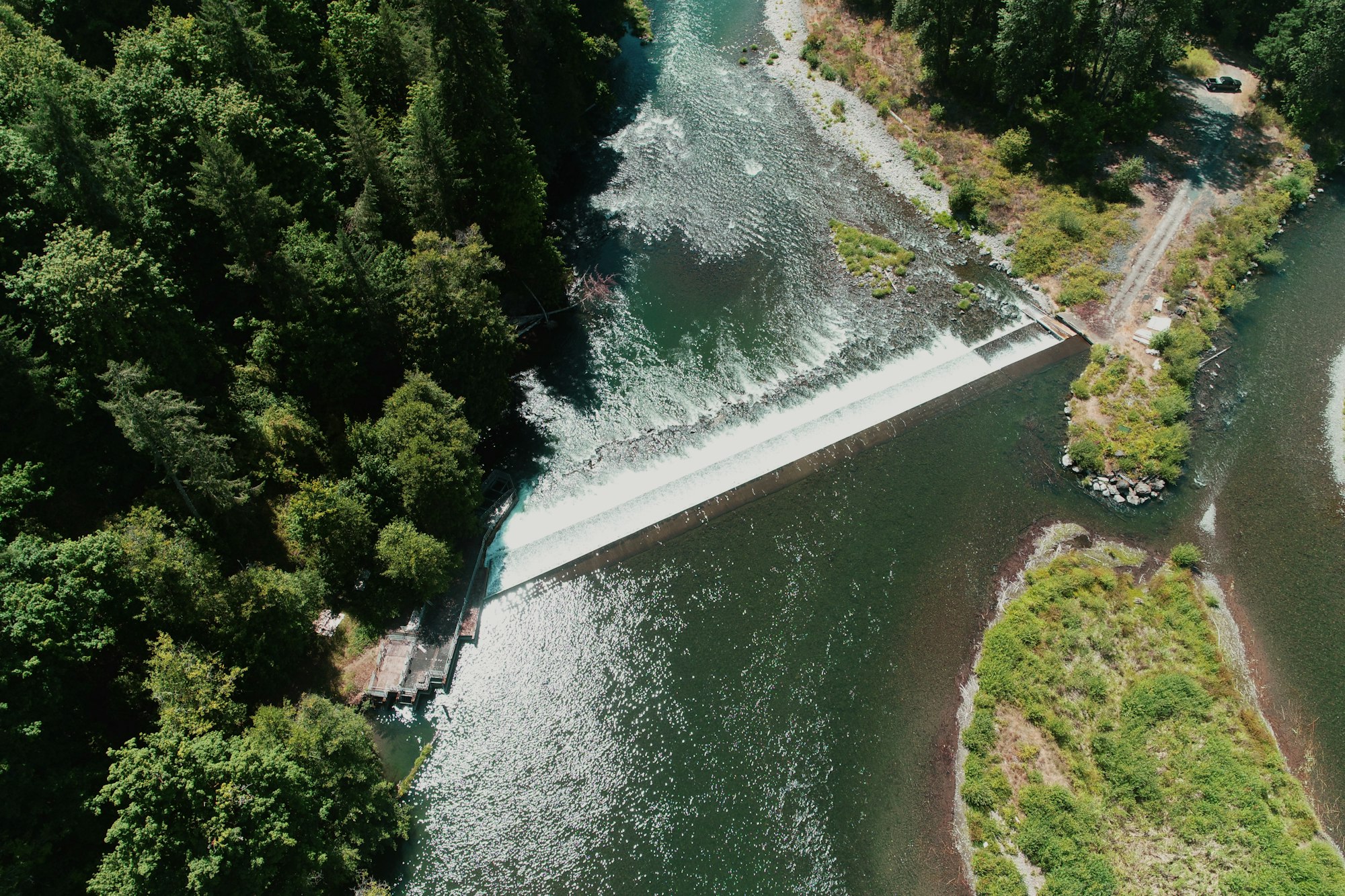 Aerial view of a dam with water cascading over it, flanked by lush greenery.