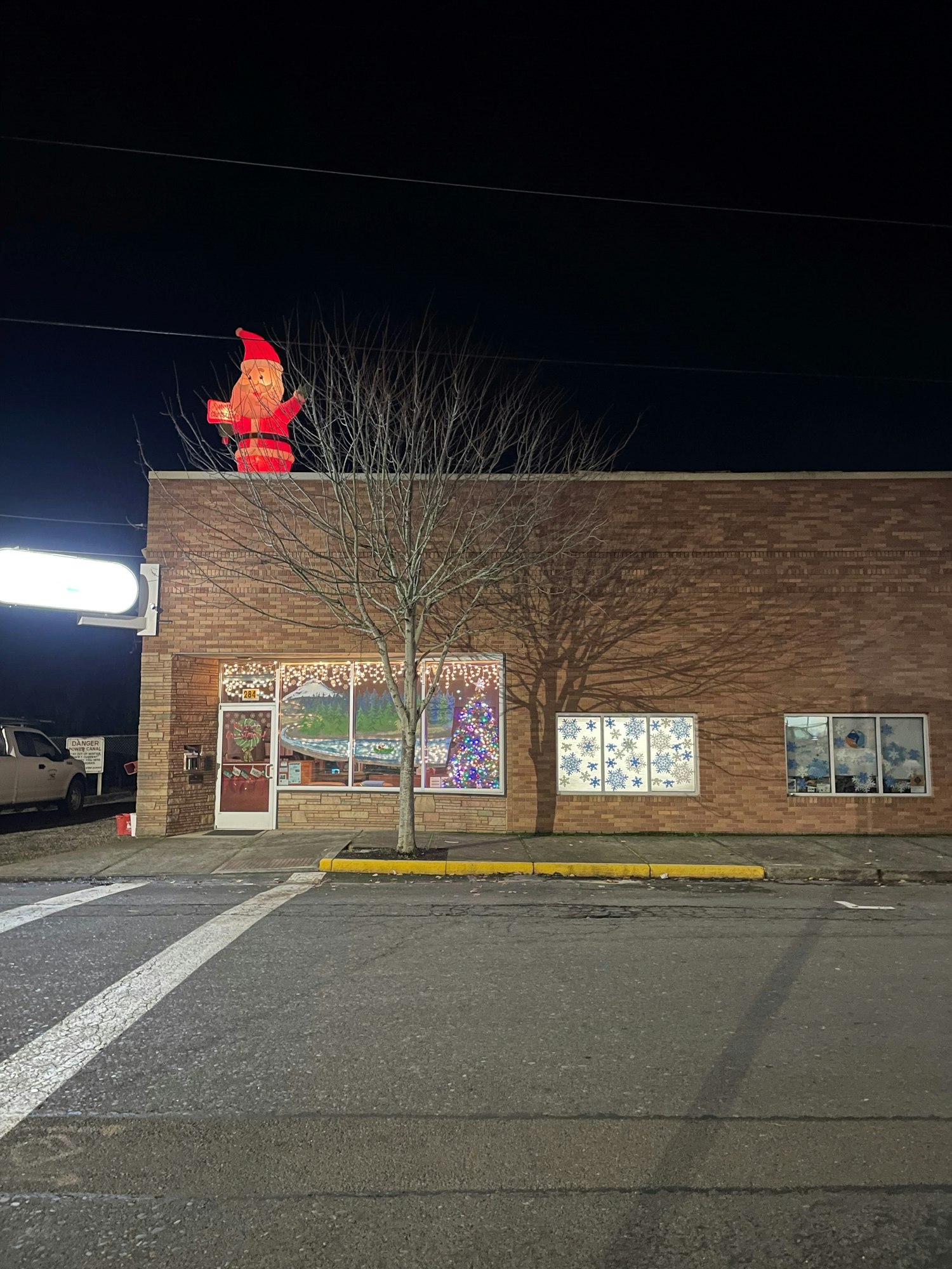 A building with holiday window decorations and an inflatable Santa on the roof at night.