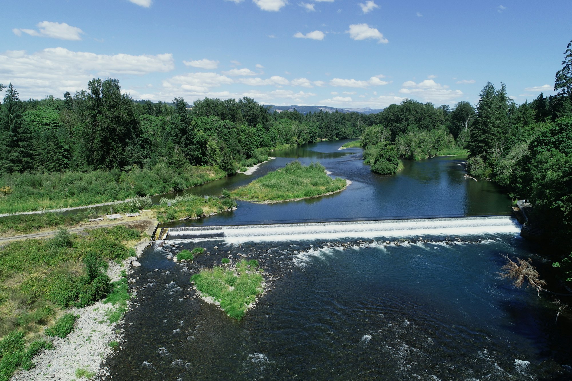 A serene river landscape with trees and a small dam or weir under a blue sky.