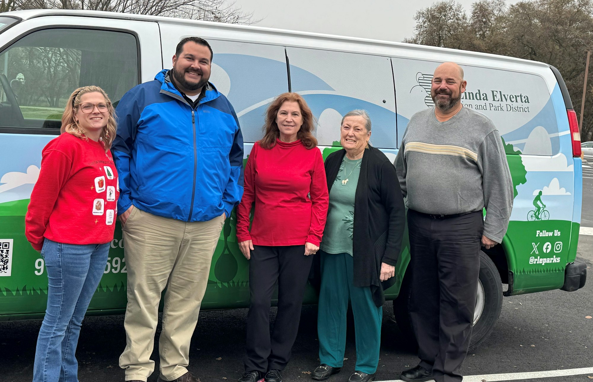 Five people standing in front of a van with a logo for a recreation and park district.