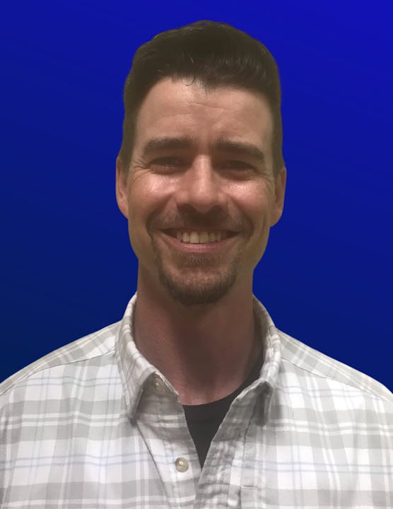 A smiling person in a plaid shirt against a blue background.