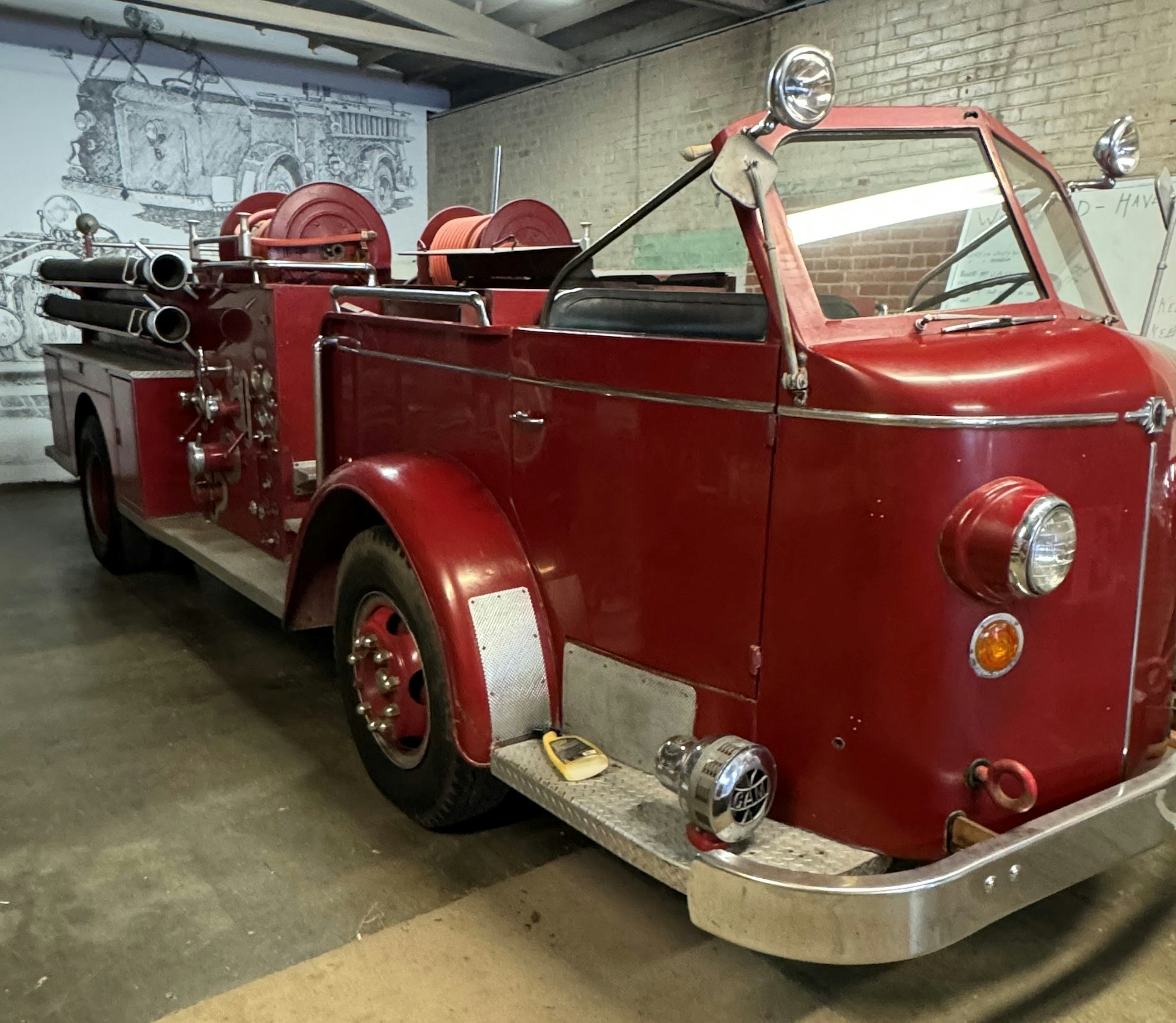 A vintage red fire truck parked indoors, featuring hoses and shiny round headlights.