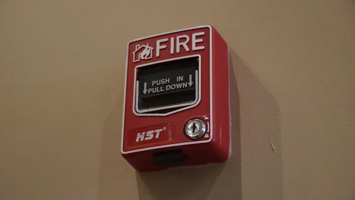 The image shows a red fire alarm pull station mounted on a wall, with instructions to "PUSH IN" and "PULL DOWN."
