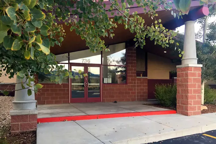 The image shows the entrance of a building with a red-bordered path, surrounded by greenery and decorative stonework.