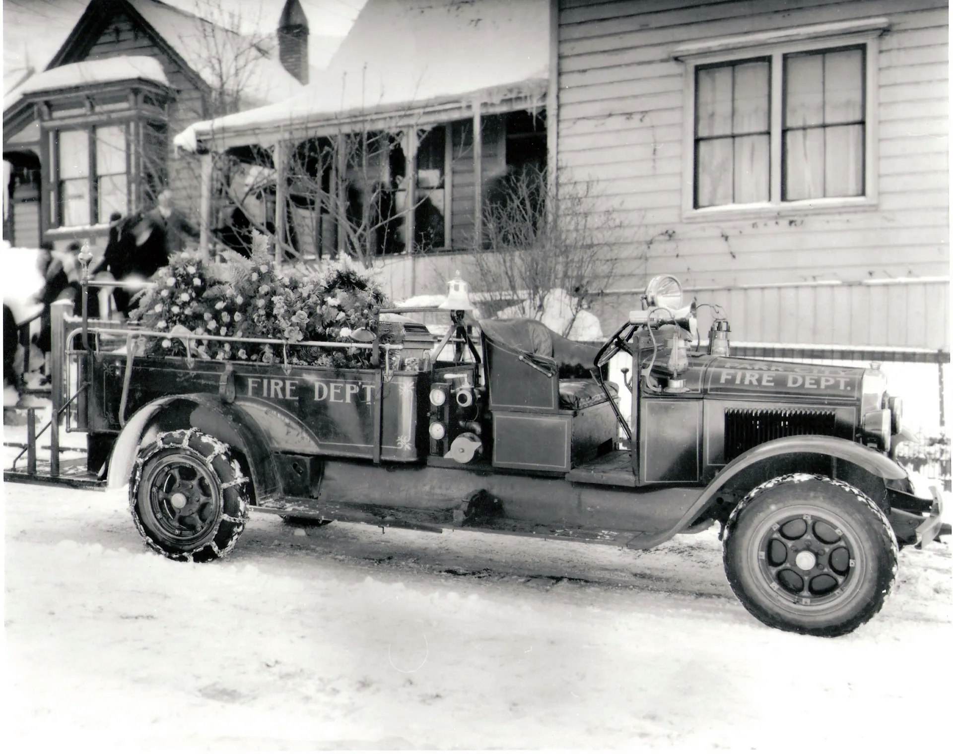 An old fire truck covered in snow, decorated with flowers, parked in front of a house during winter.