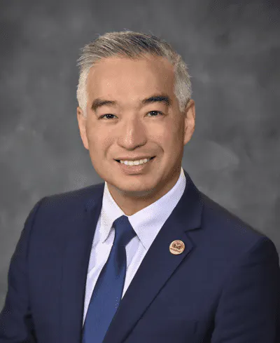 A person in a suit and tie smiling against a gray background.