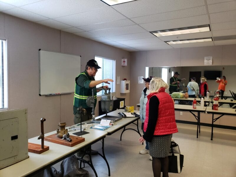 People in a room discussing or demonstrating equipment on tables.