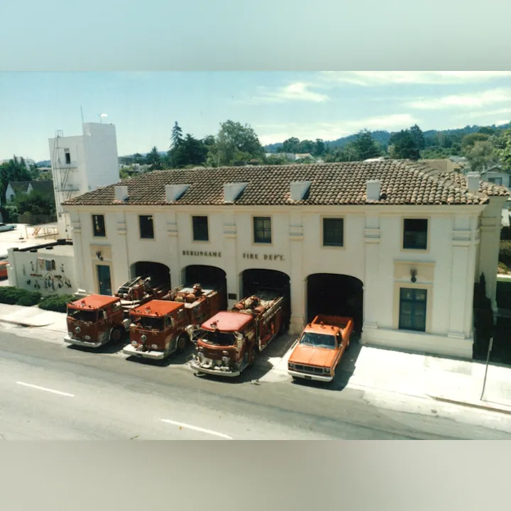 Fire station with four red fire trucks and one orange vehicle parked outside.