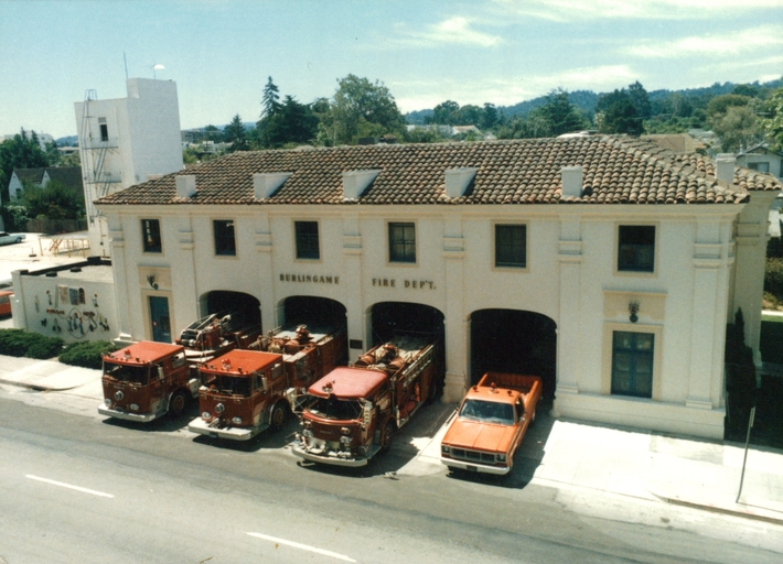 Fire station with four red fire trucks and one orange vehicle parked outside.