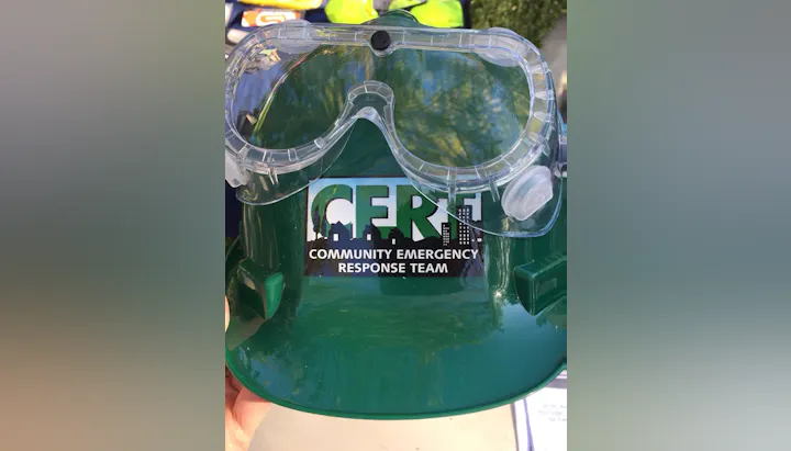 A green hard hat with clear goggles and a "Community Emergency Response Team" logo.