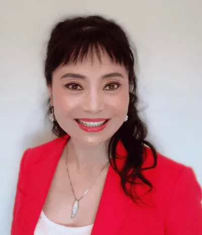 A person smiling in a red blazer, wearing a necklace and earrings.