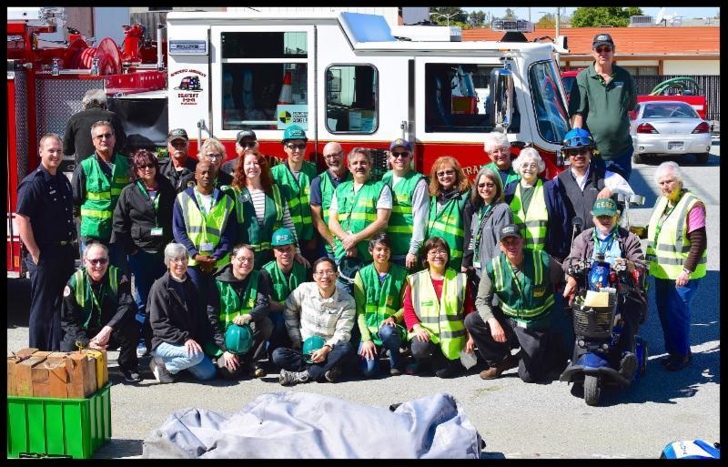 A group of people wearing green safety vests posing in front of a fire truck.