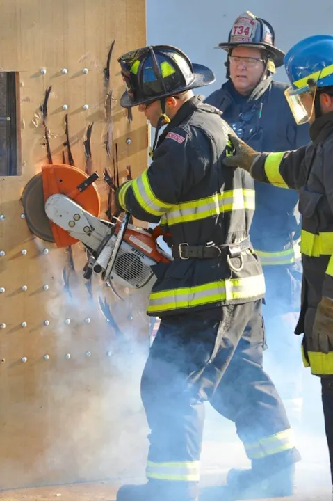 Firefighters using a power saw to cut through a wooden surface.