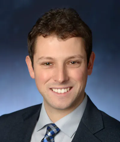 A man in formal attire smiling against a plain background.