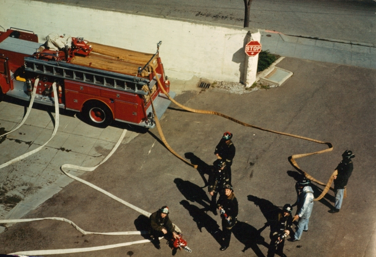 Firefighters with hoses near a red fire truck parked on the street.