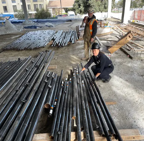 Construction site with two workers organizing metal pipes on the ground.