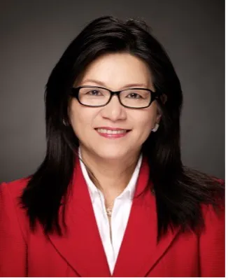 A person with long dark hair and glasses wearing a red jacket over a white shirt, smiling against a plain background.