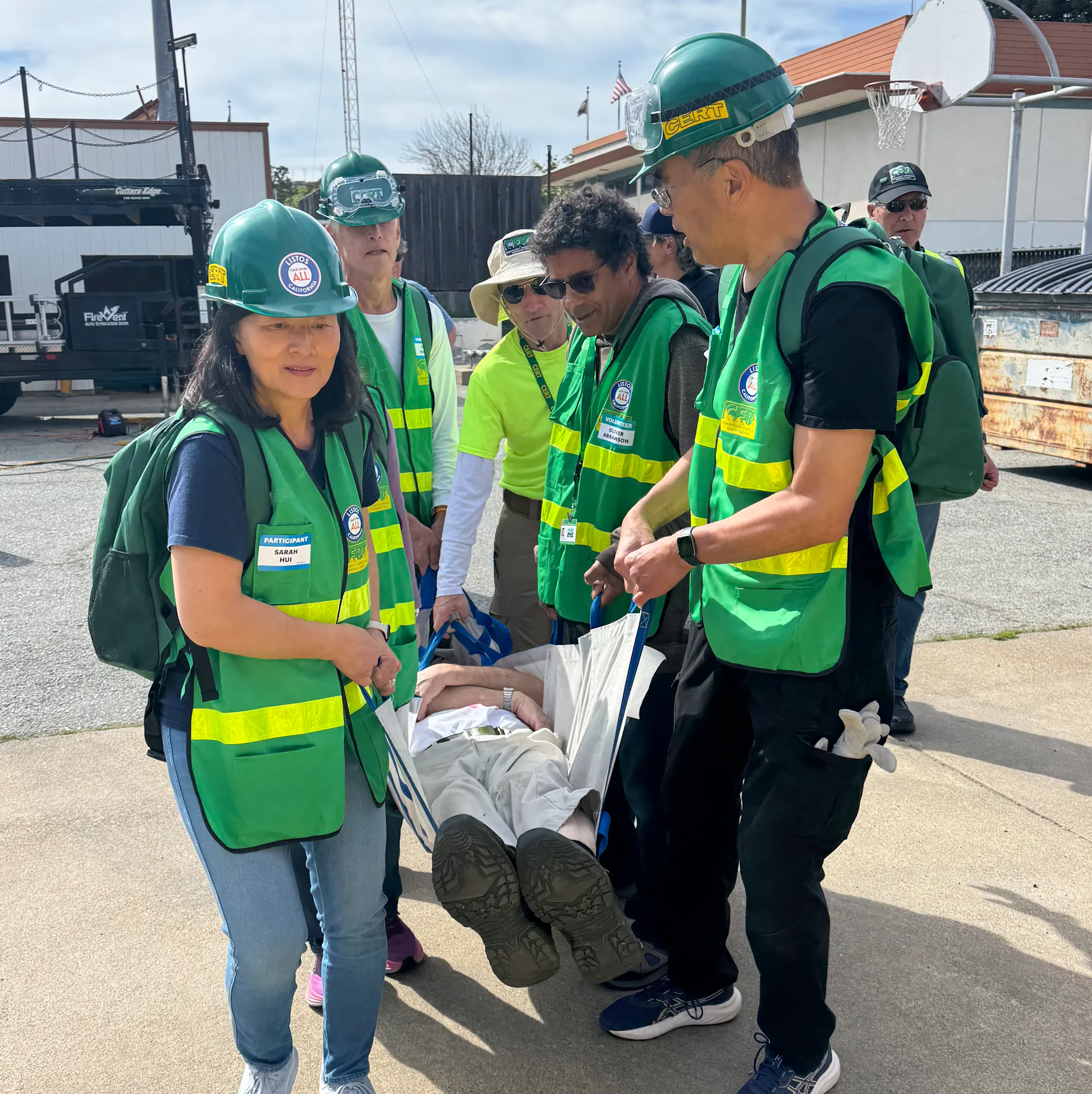 A group in safety vests and helmets is carrying a person on a stretcher, likely participating in a training or emergency drill.