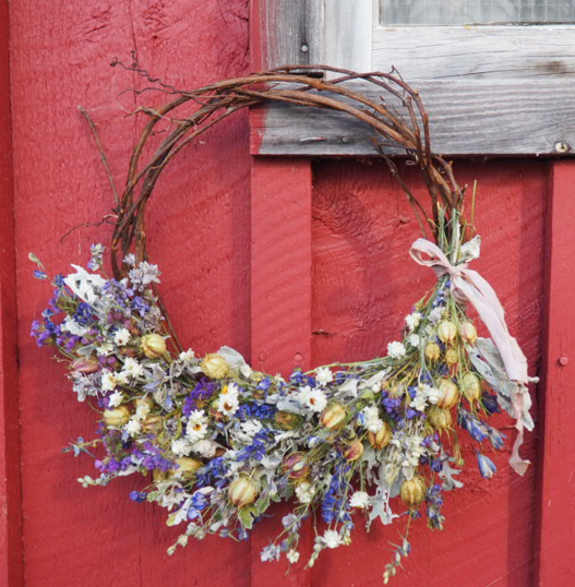 A rustic wreath with dried flowers, tied with a ribbon, on a red wooden wall.