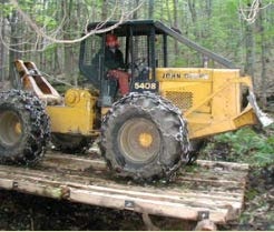 A person operates a yellow skidder in the woods.