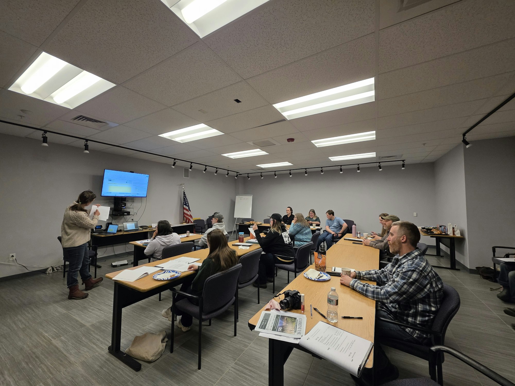 A group of people attending a presentation in a conference room, with a speaker and multiple laptops in use.