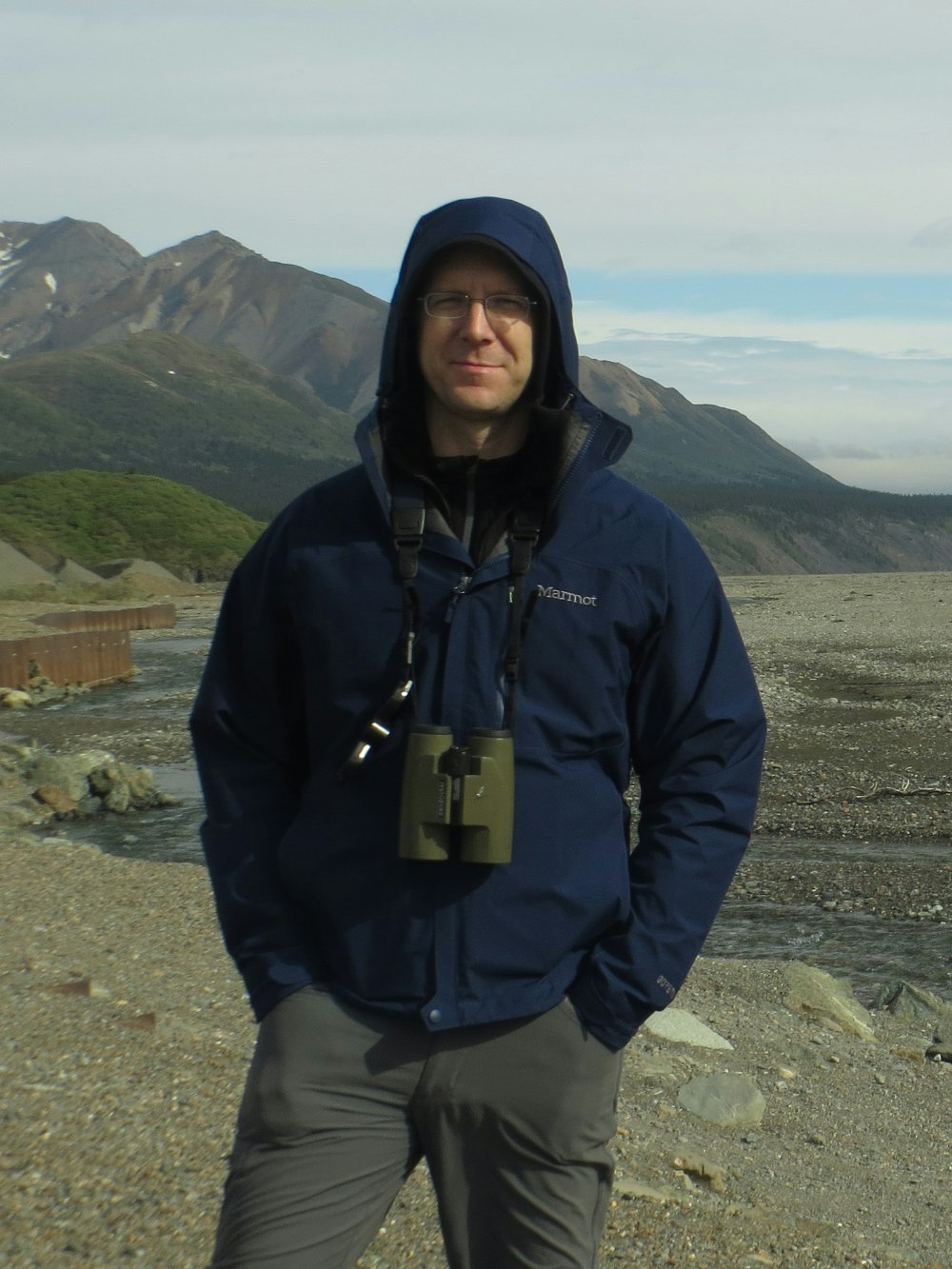 A person with binoculars standing in front of mountains.