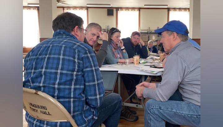People gathered around a table, engaged in a discussion at a town hall meeting.