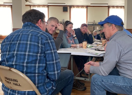 People gathered around a table, engaged in a discussion at a town hall meeting.