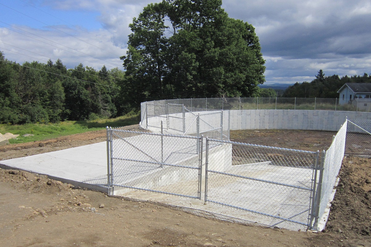 A fenced concrete slab and cinder block walls under construction, with trees and clouds in the background.