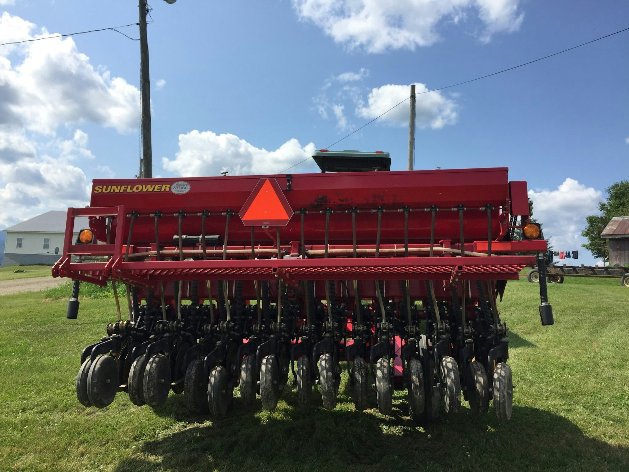 A red agricultural seed drill for planting crops, parked on grass with a clear blue sky.