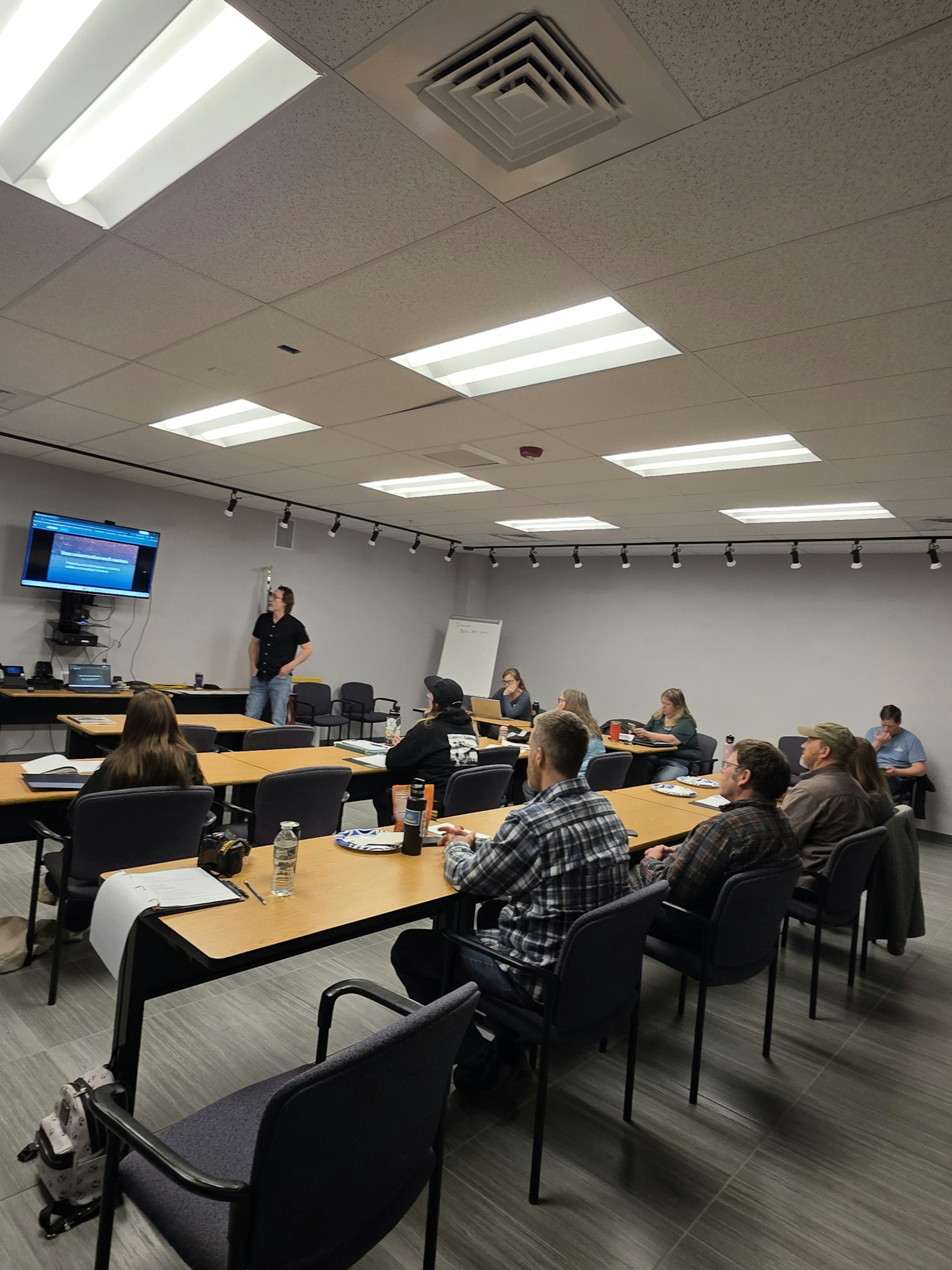 A group of people are seated in a conference room, listening to a presentation while taking notes.