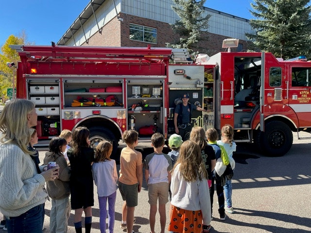 May contain: person, clothing, footwear, shoe, adult, female, woman, fire truck, transportation, truck, vehicle, hat, accessories, bag, handbag, and glove