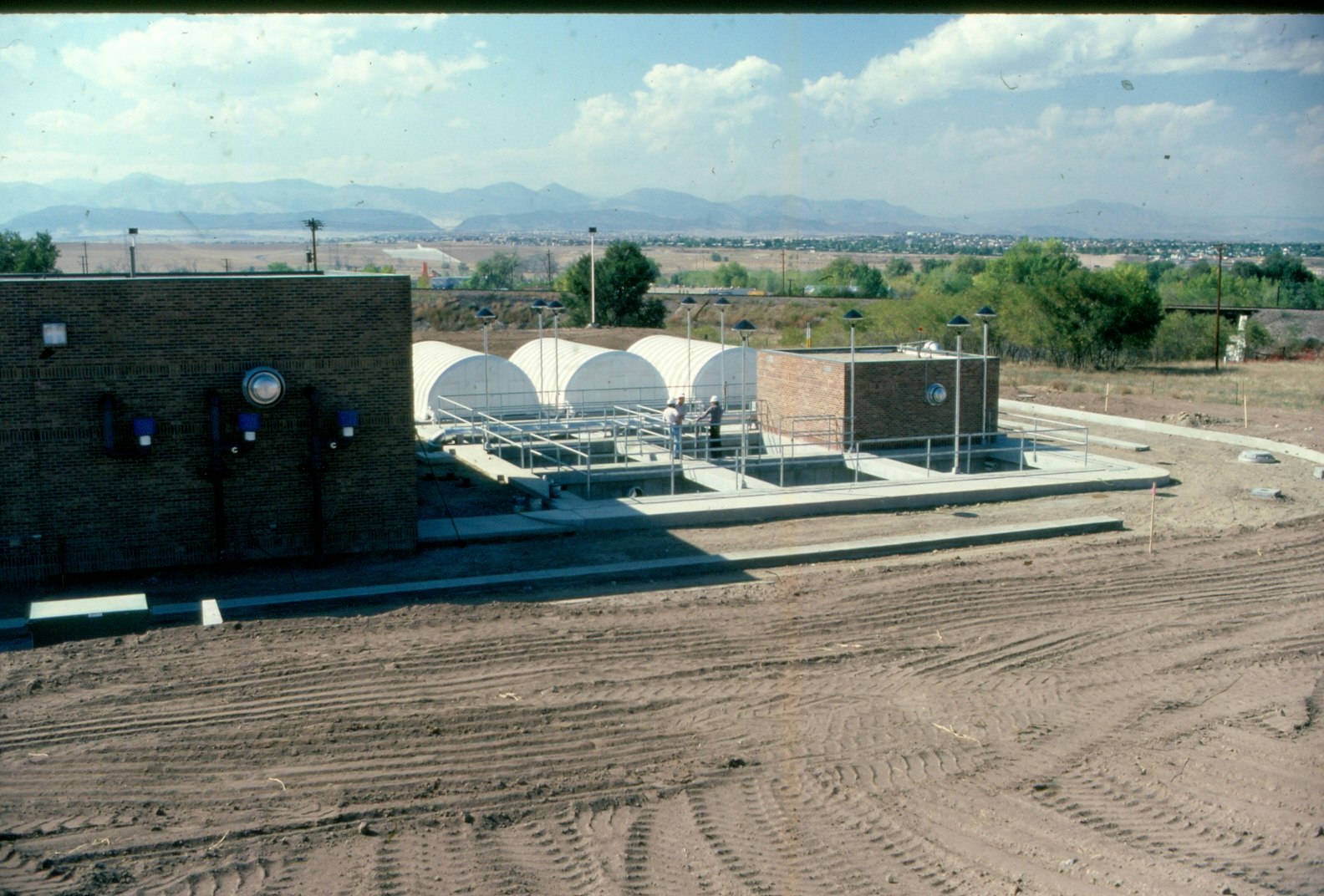 A wastewater treatment facility with buildings and structures, with mountains in the background.